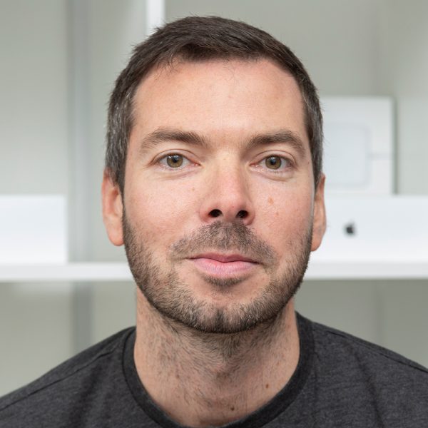 Andy Hitchman, freelance web designer head shot - smiling, standing in front of shelving unit