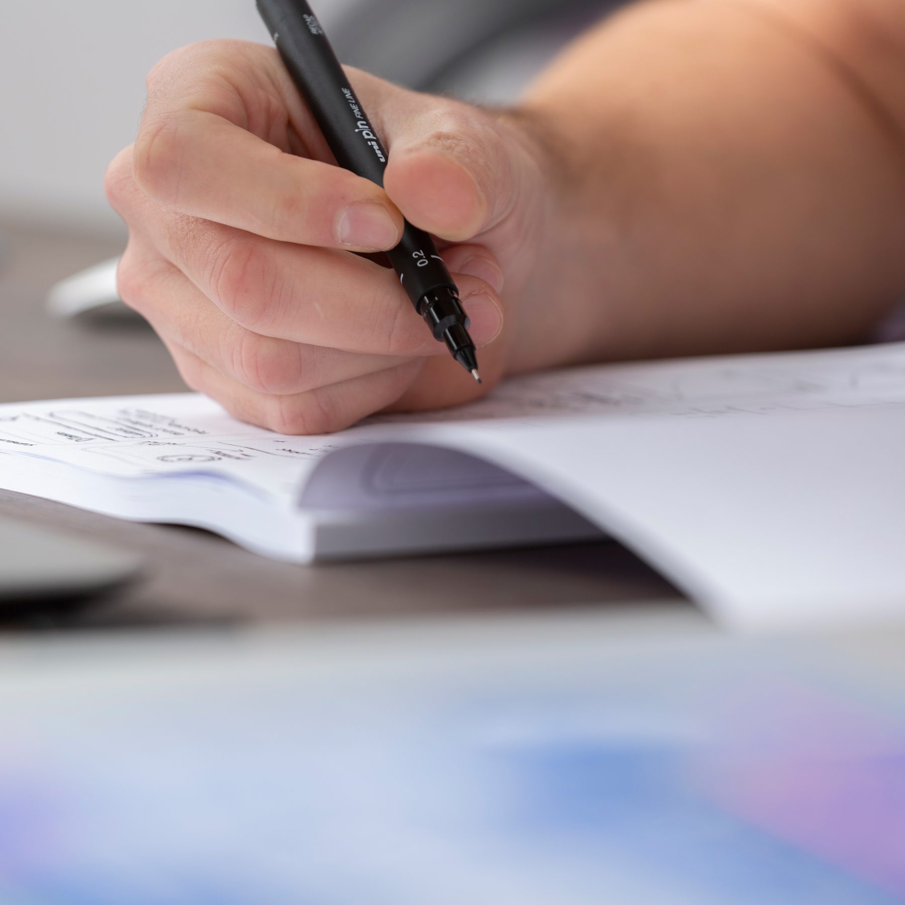 Close-up of freelance web designer Andy's hand grasping graphic pen that's hovering over a sketchbook